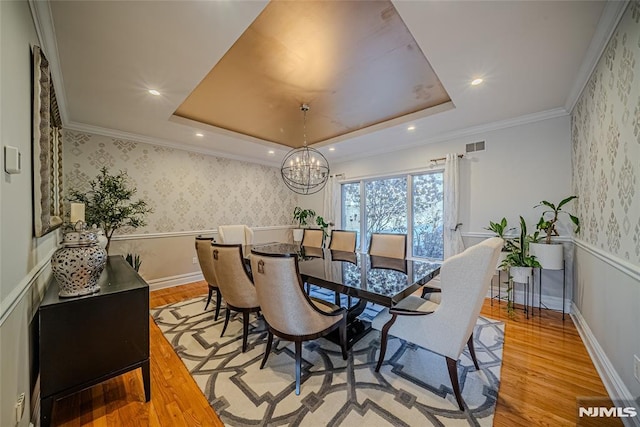 dining space with a tray ceiling, crown molding, a chandelier, and light wood-type flooring