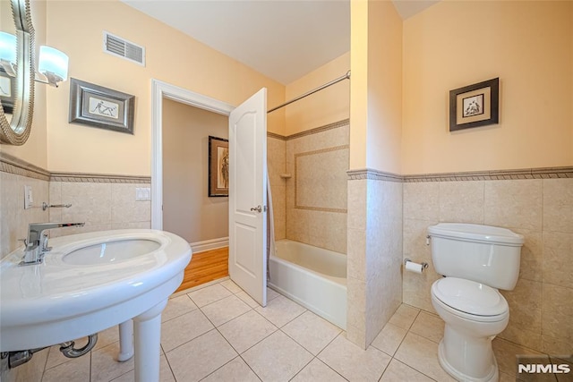 full bathroom with tile patterned floors, sink, tiled shower / bath, toilet, and tile walls