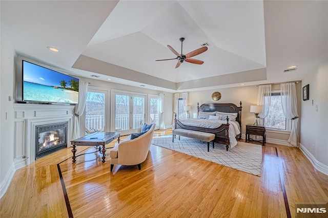 bedroom featuring a raised ceiling, ceiling fan, and light hardwood / wood-style flooring