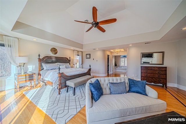 bedroom featuring ceiling fan, light hardwood / wood-style floors, a raised ceiling, and multiple windows