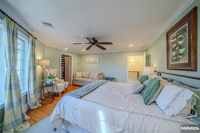 bedroom with a walk in closet, ceiling fan, crown molding, light hardwood / wood-style floors, and a closet