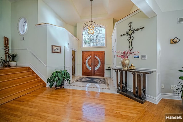 foyer with light hardwood / wood-style floors, a towering ceiling, and a chandelier