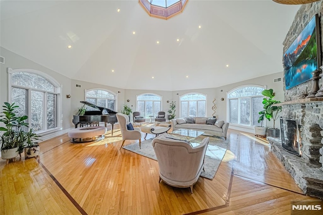 living room featuring high vaulted ceiling, a stone fireplace, and light hardwood / wood-style floors