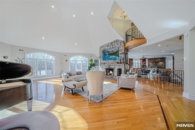 living room featuring a stone fireplace, a high ceiling, and light wood-type flooring