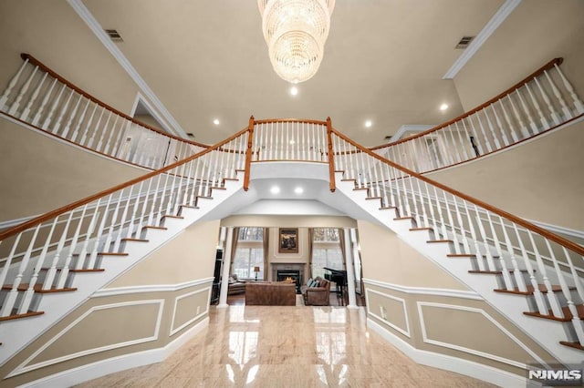 staircase with crown molding, a high ceiling, and an inviting chandelier