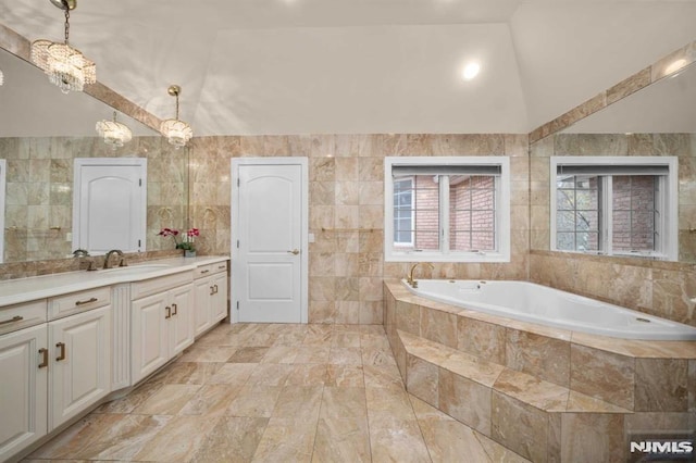 bathroom with vanity, tile walls, tiled bath, and a chandelier