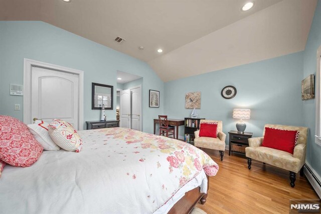 bedroom featuring a closet, light wood-type flooring, a baseboard radiator, and vaulted ceiling