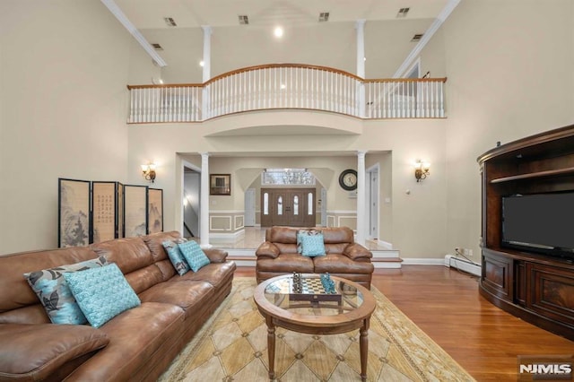 living room with wood-type flooring, ornate columns, baseboard heating, and ornamental molding