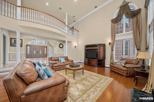 living room featuring decorative columns, ornamental molding, a baseboard heating unit, light hardwood / wood-style flooring, and a high ceiling