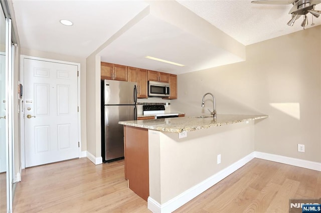 kitchen featuring sink, light stone counters, light wood-type flooring, appliances with stainless steel finishes, and kitchen peninsula