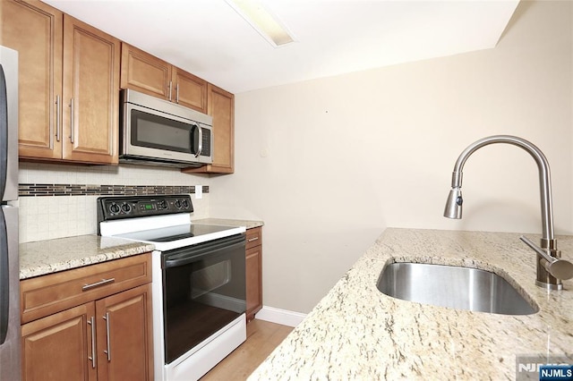 kitchen with sink, decorative backsplash, light stone counters, light wood-type flooring, and electric stove