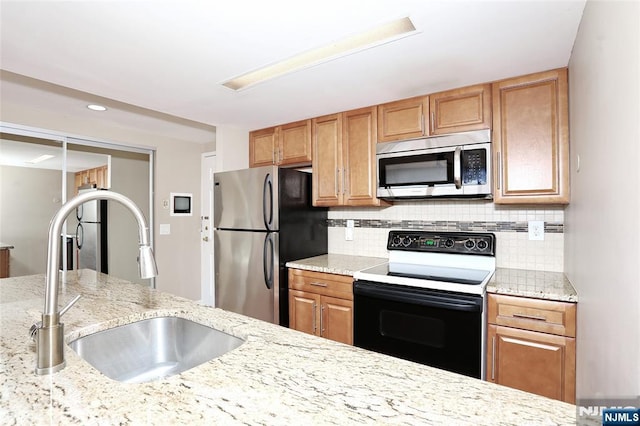 kitchen with light stone counters, stainless steel appliances, sink, and decorative backsplash