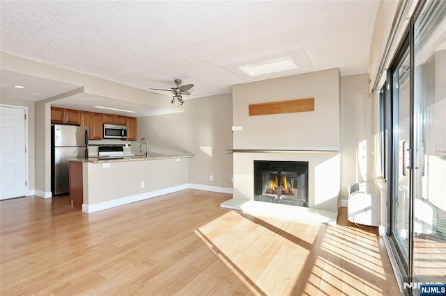 unfurnished living room featuring ceiling fan, sink, a textured ceiling, and light hardwood / wood-style floors