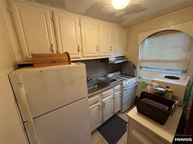 kitchen with backsplash, sink, light tile patterned floors, white appliances, and white cabinets