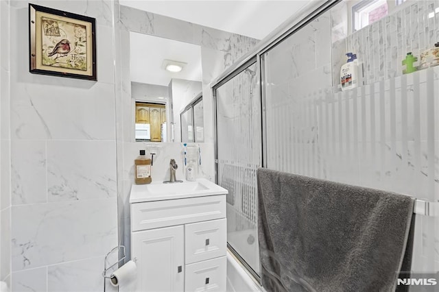 bathroom with shower / bath combination with glass door, vanity, and tile walls