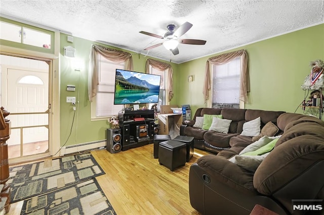 living room with ceiling fan, baseboard heating, wood-type flooring, a textured ceiling, and ornamental molding