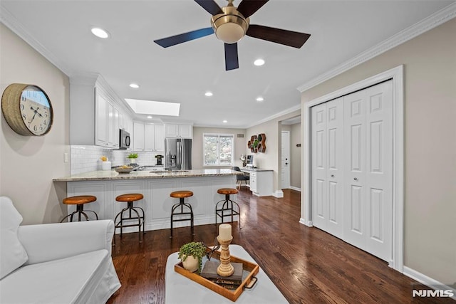 kitchen featuring white cabinets, stainless steel appliances, tasteful backsplash, a kitchen breakfast bar, and kitchen peninsula