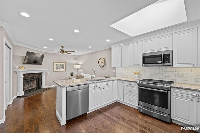 kitchen with kitchen peninsula, decorative backsplash, sink, stainless steel appliances, and white cabinets