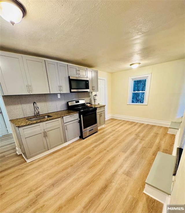 kitchen featuring backsplash, sink, light hardwood / wood-style flooring, gray cabinets, and appliances with stainless steel finishes