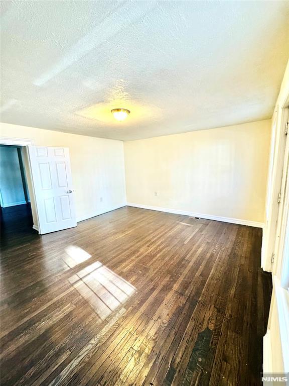 unfurnished room with a textured ceiling and dark wood-type flooring