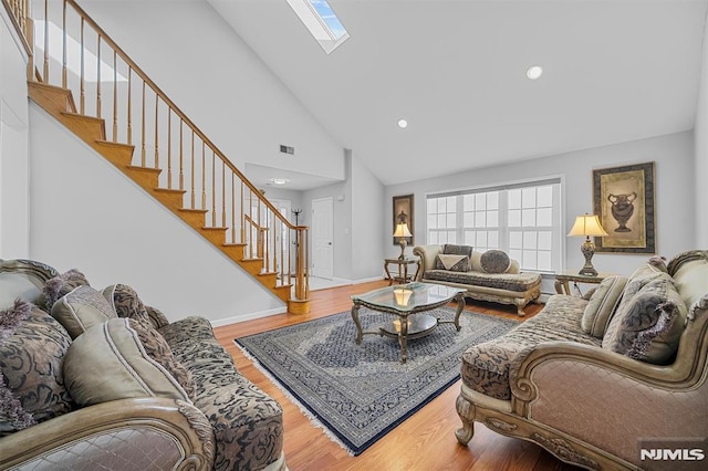 living room featuring hardwood / wood-style flooring, high vaulted ceiling, and a skylight