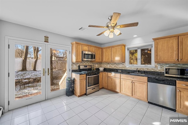 kitchen featuring sink, ceiling fan, dark stone countertops, light tile patterned floors, and stainless steel appliances