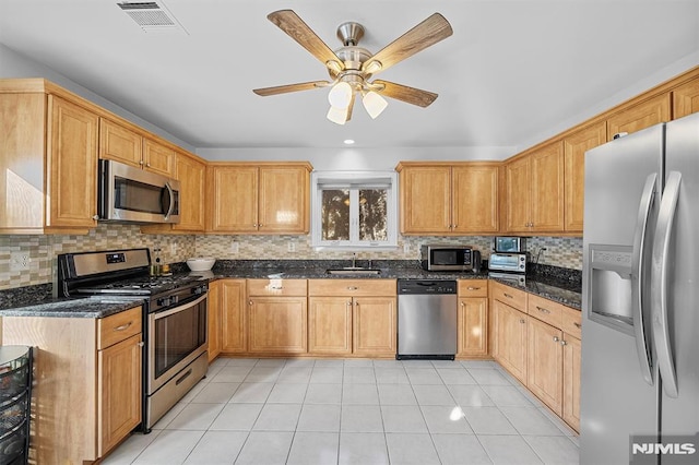 kitchen featuring sink, ceiling fan, dark stone countertops, light tile patterned floors, and appliances with stainless steel finishes