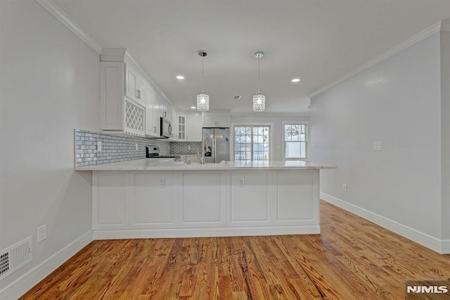 kitchen with white cabinetry, kitchen peninsula, pendant lighting, crown molding, and appliances with stainless steel finishes