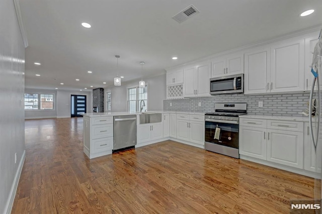 kitchen with white cabinets, stainless steel appliances, kitchen peninsula, pendant lighting, and sink