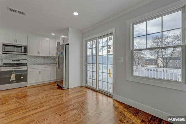 kitchen with light hardwood / wood-style floors, crown molding, backsplash, white cabinetry, and appliances with stainless steel finishes