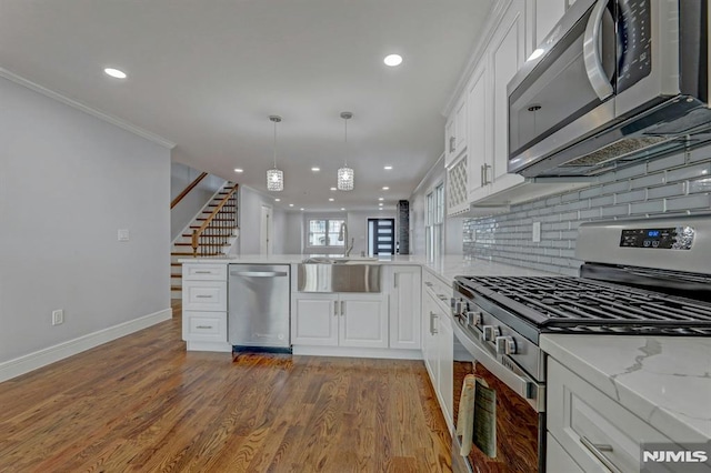 kitchen with stainless steel appliances, sink, white cabinetry, kitchen peninsula, and pendant lighting