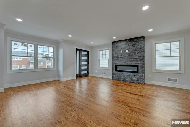 unfurnished living room with a healthy amount of sunlight, light wood-type flooring, a stone fireplace, and crown molding