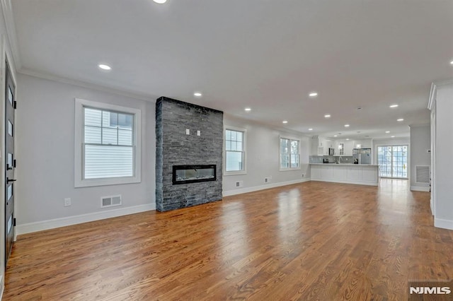 unfurnished living room featuring ornamental molding, light wood-type flooring, and a stone fireplace