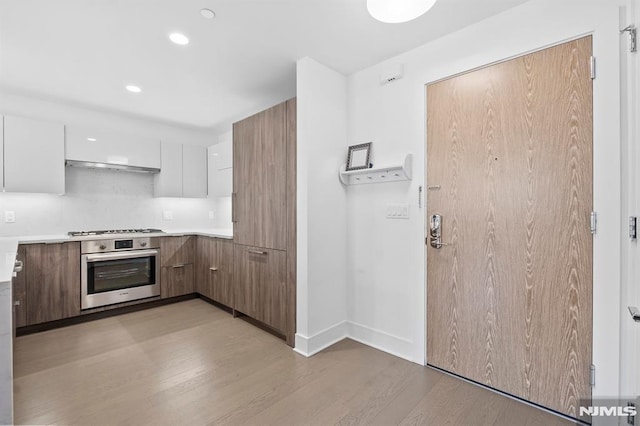 kitchen featuring white cabinets, backsplash, light hardwood / wood-style floors, and stainless steel appliances