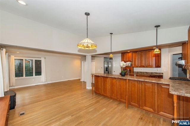 kitchen featuring lofted ceiling, pendant lighting, stainless steel refrigerator with ice dispenser, light wood-type flooring, and light stone countertops