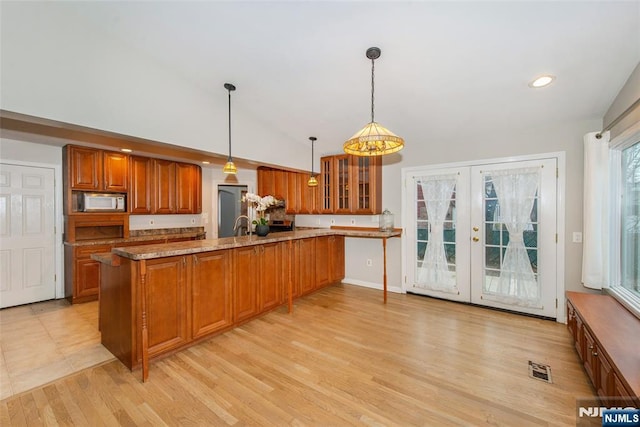 kitchen with lofted ceiling, french doors, hanging light fixtures, light hardwood / wood-style flooring, and light stone counters