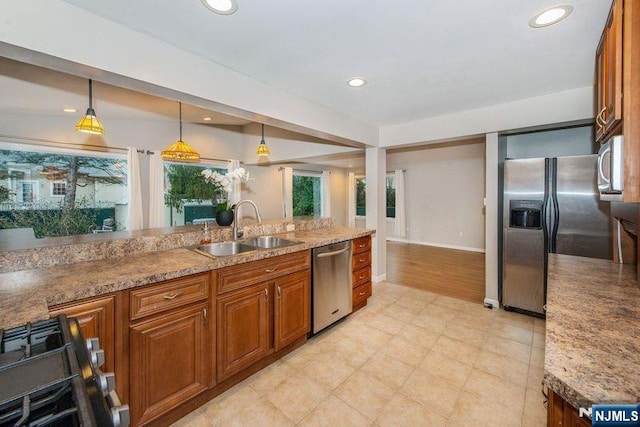 kitchen featuring hanging light fixtures, light stone countertops, appliances with stainless steel finishes, and sink