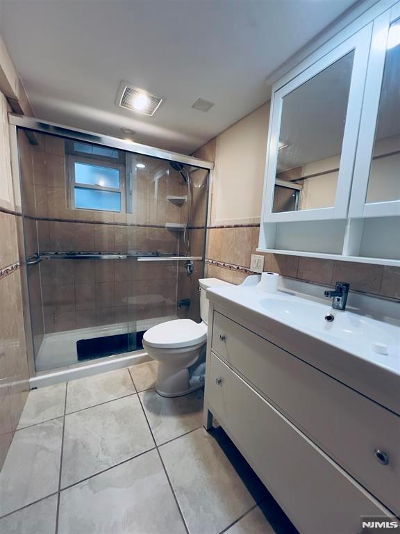 bathroom with tile patterned floors, vanity, a shower with door, tile walls, and toilet