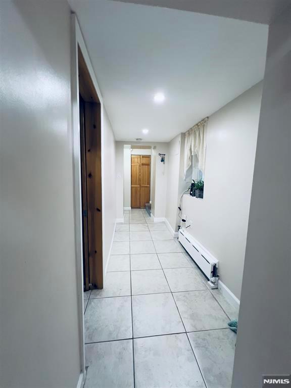 hall with light tile patterned floors and a baseboard heating unit