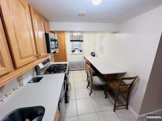 kitchen with light brown cabinetry, radiator heating unit, stainless steel appliances, and sink