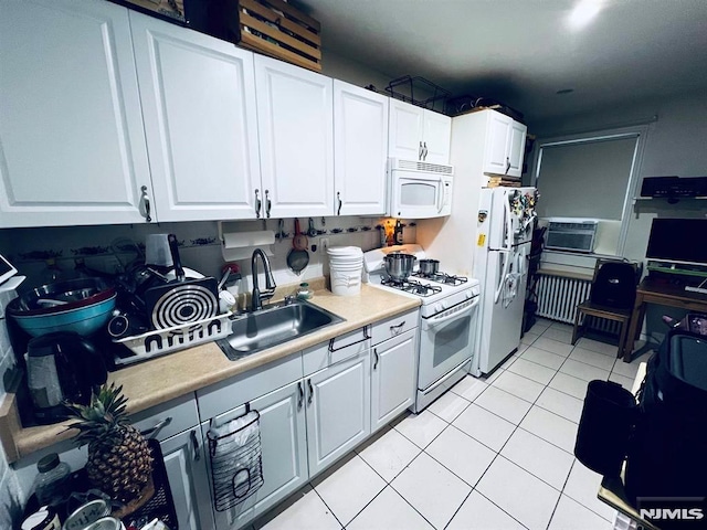 kitchen featuring white appliances, sink, light tile patterned floors, radiator heating unit, and white cabinetry