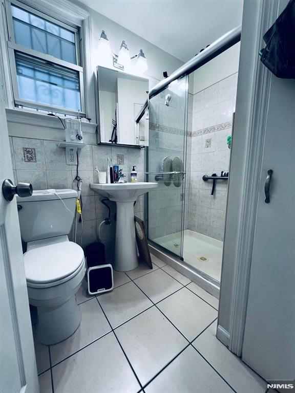 bathroom with a shower with door, sink, tile walls, tile patterned flooring, and toilet