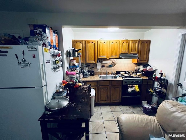 kitchen with sink, white refrigerator, black gas stove, decorative backsplash, and light tile patterned flooring