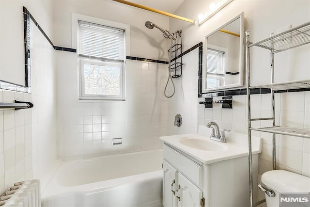 full bathroom featuring vanity, tiled shower / bath combo, toilet, tile walls, and radiator heating unit