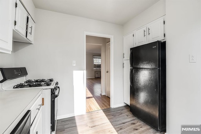 kitchen featuring black fridge, stainless steel dishwasher, gas range oven, light wood-type flooring, and white cabinetry