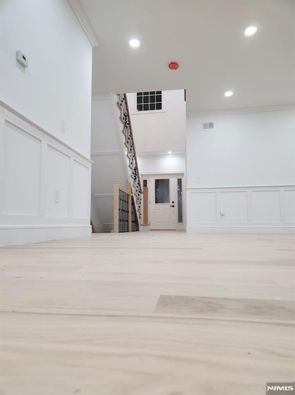 unfurnished living room with crown molding, recessed lighting, visible vents, a decorative wall, and stairs