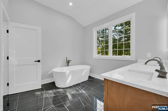 bathroom featuring double vanity, baseboards, lofted ceiling, a freestanding tub, and a sink