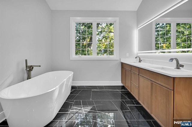 bathroom with a soaking tub, a sink, baseboards, and double vanity