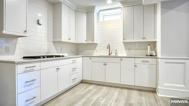 kitchen with sink, white cabinets, decorative backsplash, and light hardwood / wood-style flooring