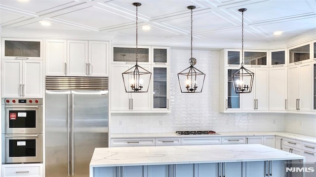 kitchen with light stone countertops, hanging light fixtures, a center island, white cabinets, and appliances with stainless steel finishes